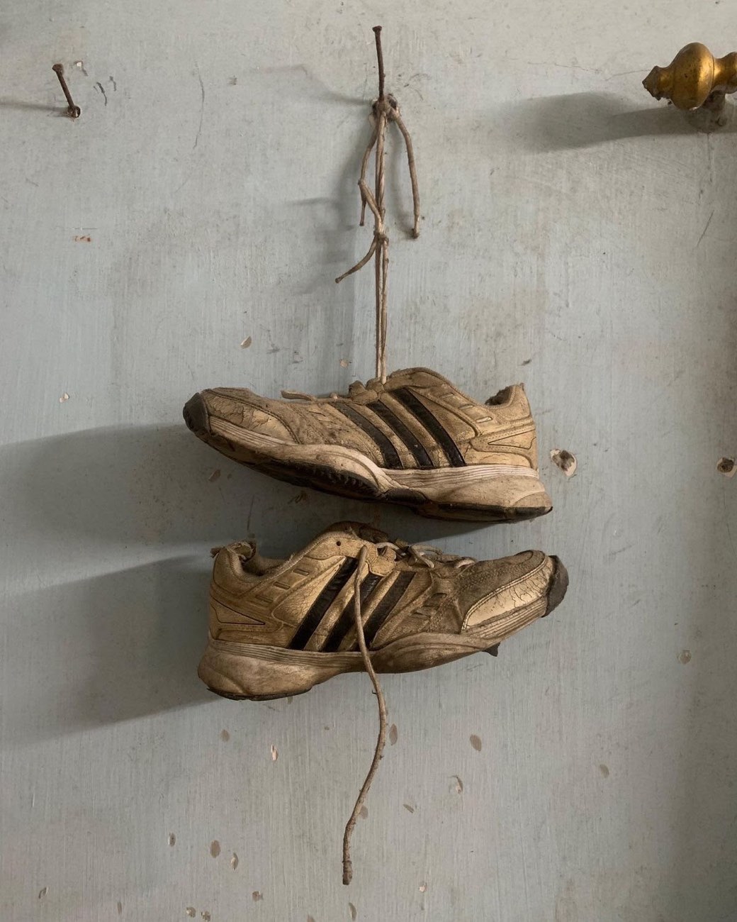 Ein Paar alte, abgetragene Turnschuhe hängt an einem Nagel an der Wand